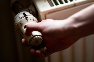 Eine Hand dumfasst den Temperaturregler eines Heizkörpers