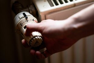 Eine Hand dumfasst den Temperaturregler eines Heizkörpers