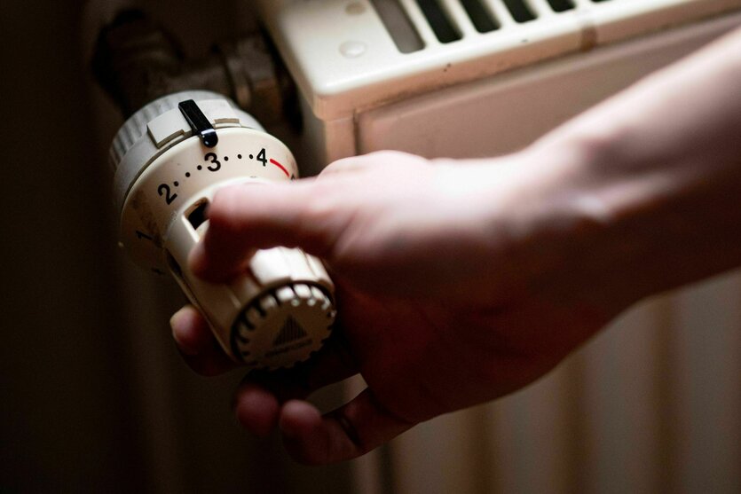 Eine Hand dumfasst den Temperaturregler eines Heizkörpers