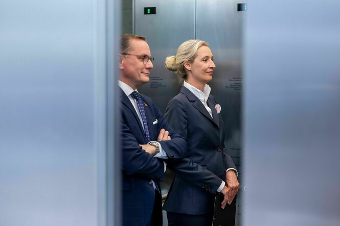 Tino Chrupalla und Alice Weidel stehen grinsend in einem Fahrstuhl