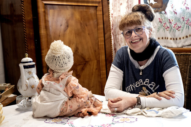 Eine Frau sitz an einem Tisch auf dem ihr gegenüber ein Puppe sitzt