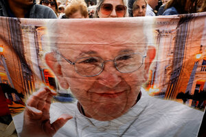 Eine Frau mit Sonnenbrille steht hinter einem Plakat mit dem Gesicht von Papst Franziskus
