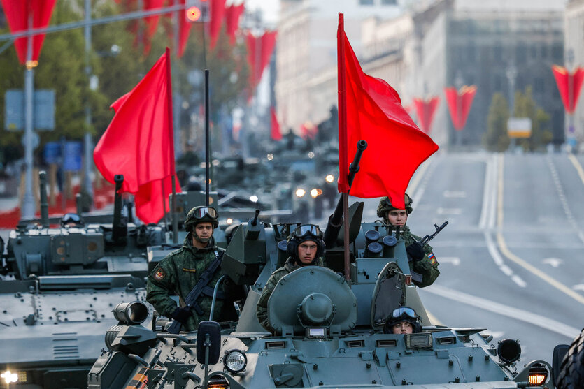 Innenstadt von Moskau, auf dem großen Boulevard fahren Panzer in Kolonne, die mit roten Fahnen geschmückt sind. Im Vordergrund drei Soldaten, die auf dem Panzer stehen