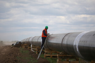 Ein Bauarbeiter steht auf einer an einer Pipeline gelehnten Leiter