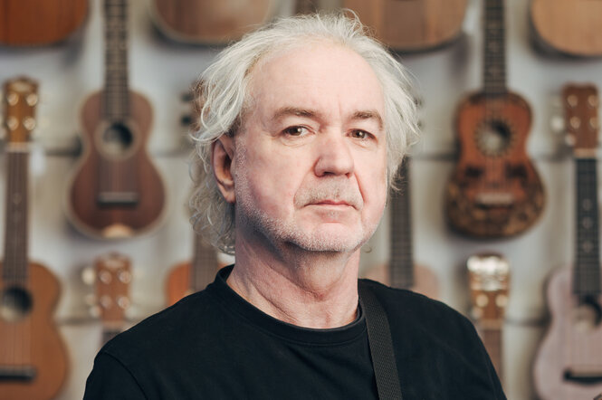 Ein Mann steht vor einer Wand an der einige Ukulele hängen