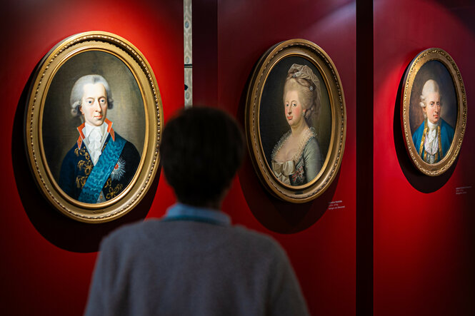 Eine Frau steht im Residenzmuseum im Celler Schloss vor Gemälden, die Christian VII, Caroline Mathilde und Johann Friedrich Struensee zeigen.