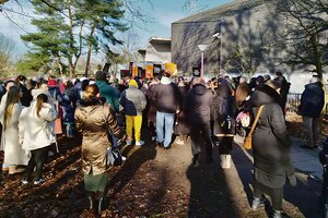 Menschen sind von hinten zu sehen. Einige tragen Transparente. Sie stehen auf einer Demo vor der Maria-Magdalena-Kirche in Hamburg Osdorf.