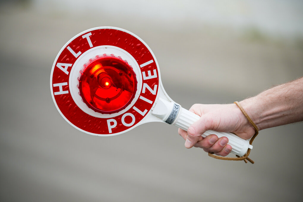 Ein Polizist hält eine Kelle mit der Aufschrift "Halt Polizei" in der Hand.