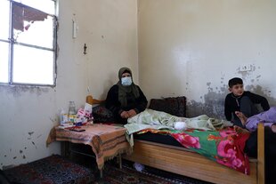 Eine Frau mit einem Beinstumpf sitzt auf einem Bett, neben ihr ein Junge, medikamente auf einem Tisch