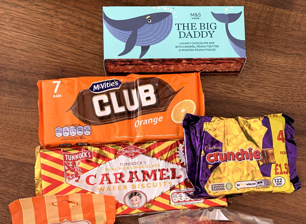 Mehrere Süßigkeiten aus Großbritannien in bunten Verpackungen liegen auf einer dunklen Holztischplatte