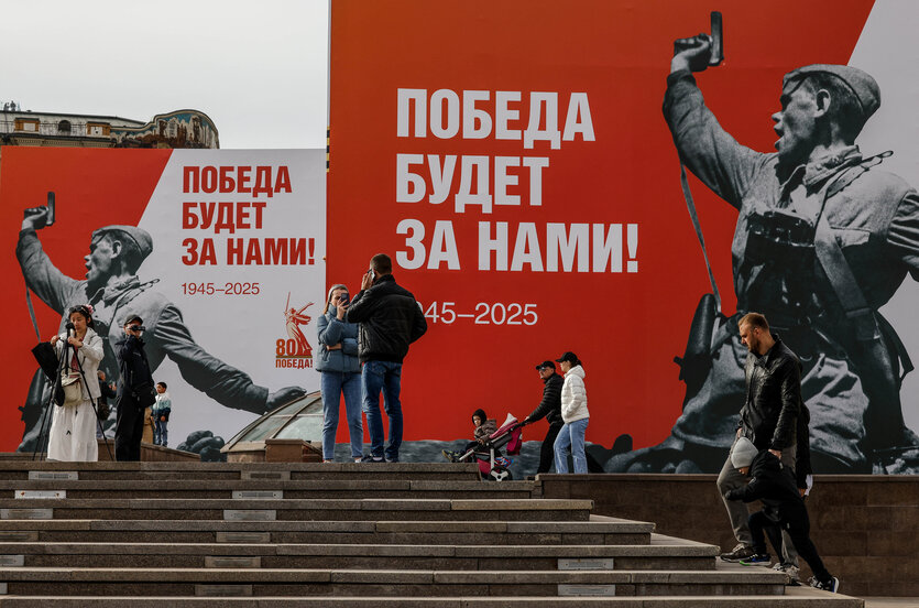 Menschen vor Plakaten mit der Aufschrift Der Sieg wird unser sein. zum Jahrestag des Sieges über Nazi-Deutschland