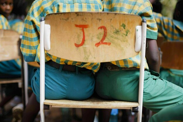 Zwei Schüler sitzen auf einem Stuhl, es ist nur ein Ausschnitt zu sehen - von der Sitzfläche bis zur Stuhllehne