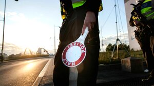 Zwei Polizisten stehen an der Straße, einer hat eine Stop-Kelle in der Hand, die andere Person hat ein Maschinengewehr in der Hand