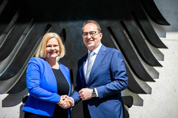 Nancy Faeser und Alexander Dobrindt stehen vor einem Bundesadler und schütteln sich die Hände. Beide lachen und sind sehr gut gelaunt