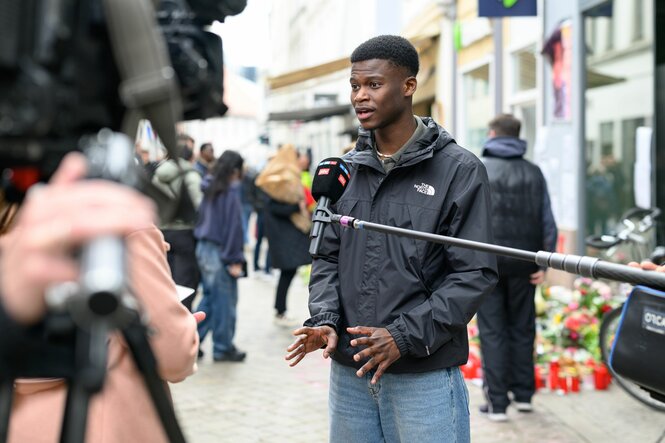 Ein junger Mann spricht auf der Straße ins Mikro von Journalisten