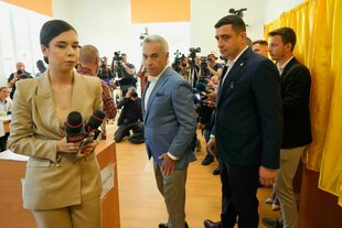 Eine Journalistin mit Mikrofonen, Calin Georgescu und George Simion umgeben von Journalisten