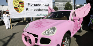 Greenpeace protestiert mit einem rosa Porsche Cayenne gegen den Autokonzern.e Cayenne Fahrzeug fährt auf einer Allee.