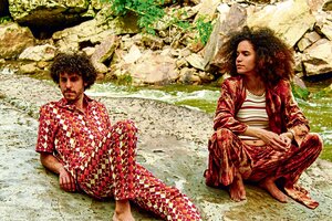 Das venezo­lanische Synth-Pop-Duo Mito y Comadre sitzend vor einem Bach