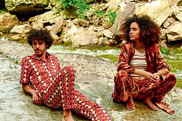 Das venezo­lanische Synth-Pop-Duo Mito y Comadre sitzend vor einem Bach