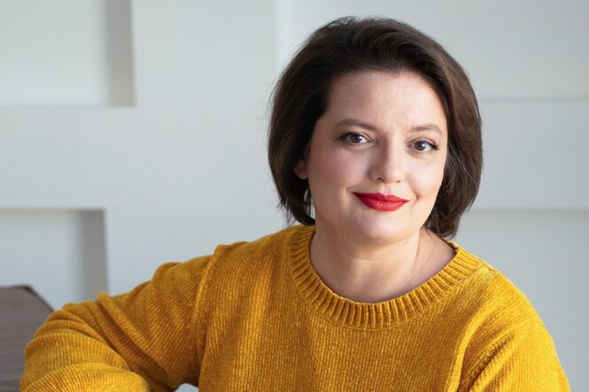 Eine Frau mit einem gelben Pullover lächelt in die Kamera