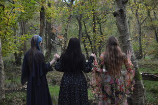 Drei Frauen in langen Kleidern im Wald, man sieht sie von hinten