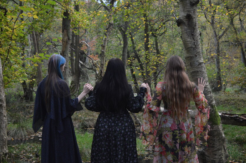 Drei Frauen in langen Kleidern im Wald, man sieht sie von hinten
