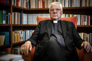 Ein katholischer Geistlicher sitzt vor einem Bücherregal