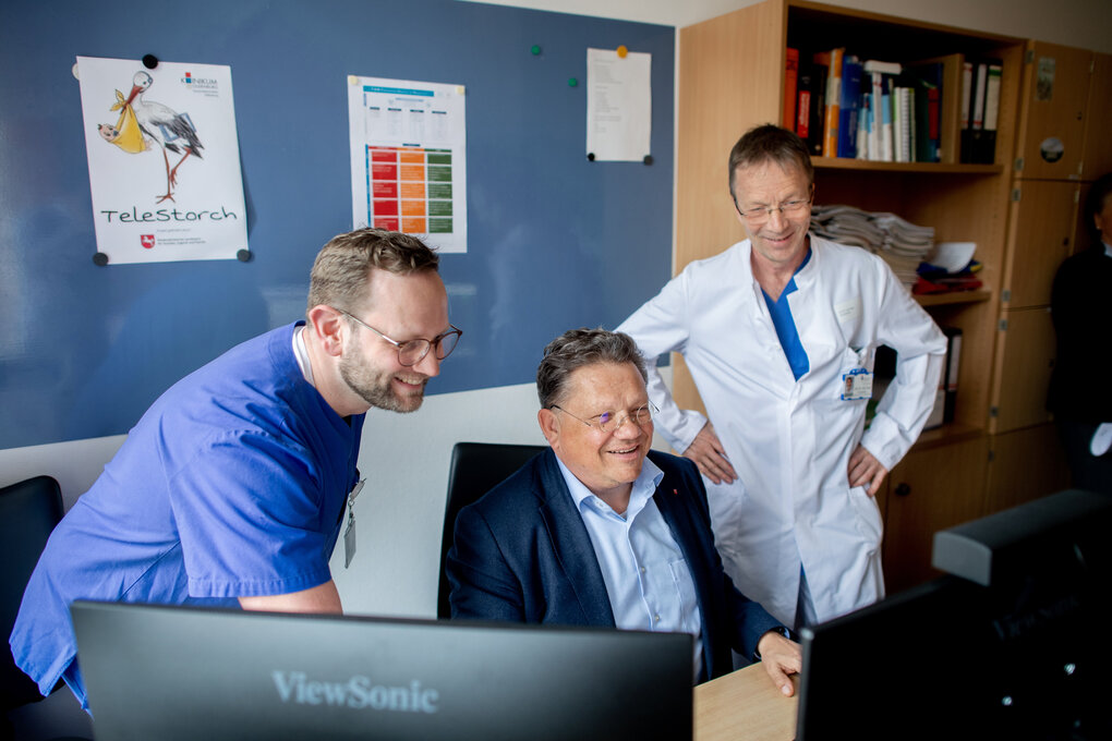 Gesundheitsminister Andreas Philippi sitzt zwischen zwei Ärzten in der Universitätsklinik für Kinder- und Jugendmedizin in Oldenburg an einem Schreibtisch und guckt auf einen Monitor.