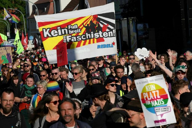 Demonstrierende halten Protestschilder hoch. Auf einem Transparent steht dabei 