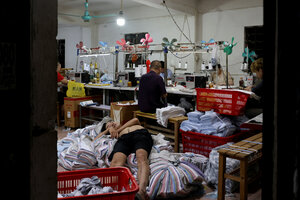 Ein Kind schläft auf einem Kleiderhaufen in einer Textrilfabrik in China.