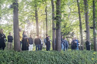 Besucher:innen stehen in der schmalen Kastanienallee im Garten des Haus der Wannsee-Konferenz und lauschen der Soundinstallation