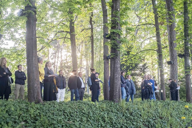 Besucher:innen stehen in der schmalen Kastanienallee im Garten des Haus der Wannsee-Konferenz und lauschen der Soundinstallation