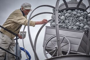 Zu sehen ist Künstler Peter Lenk, der letzte Pinselstriche auf seine Skulptur aufträgt.
