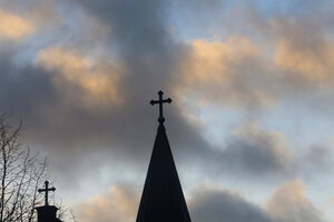Eine Kirchturmspitze mit Kreuz vor Wolkenhimmel