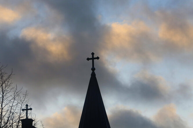 Eine Kirchturmspitze mit Kreuz vor Wolkenhimmel