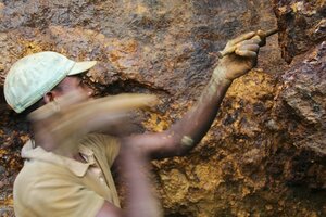 Arbeiter mit Schutzhelm schlägt Meißel in Steinwand