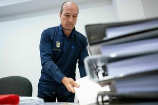 Peter Fitzek in einem Gerichtssaal hinter zahlreichen Aktenordnern, er trägt ein Hemd, auf dem "Königreich Deutschland" eingestickt ist