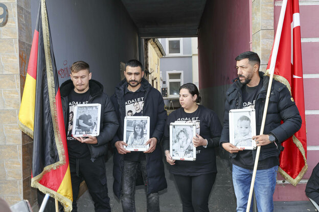 Vier Personen zeigen Fotos von einer Familie, die bei einem Brandanschlag ums Leben kamen