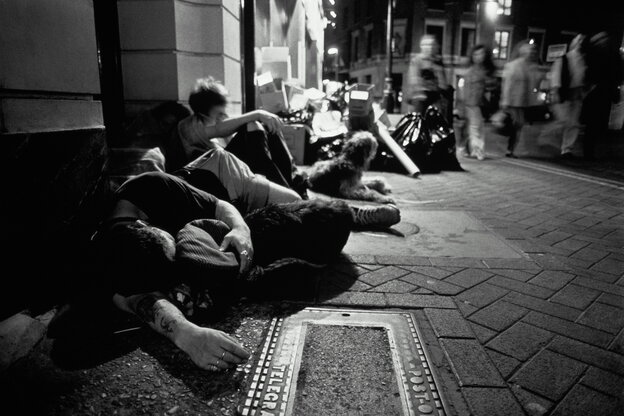 Jugendliche sitzen und schlafen auf einem Bürgersteig, Passanten laufen vorbei