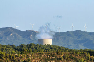 Qualmendes Atomkraftwerk vor Bergkulisse und Windrädern