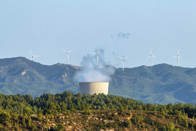 Qualmendes Atomkraftwerk vor Bergkulisse und Windrädern