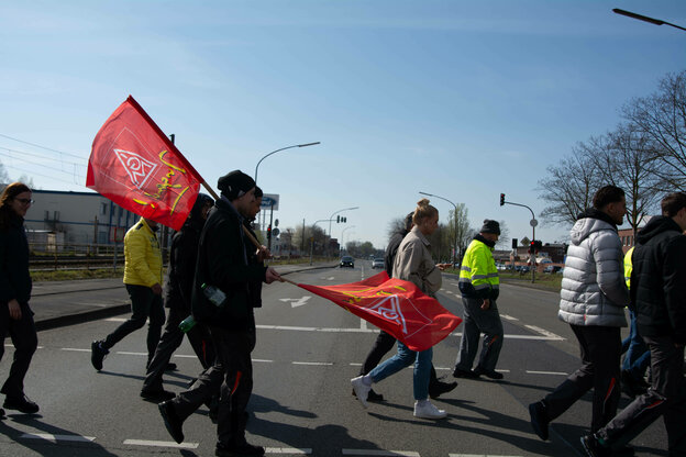 Mehrere Personen gehen über eine Straße. Einige tragen rote Fahnen
