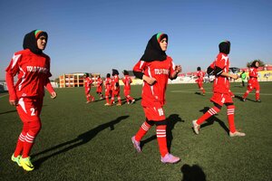 Spielerinnen mit roten Trikots und schwarzen Kopftüchern laufen über den Rasen