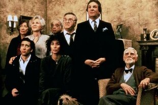 Filmszene: Loretta, Ronny und Lorettas Familie samt Hunden sind in einem Wohnzimmer versammelt. Sie schauen alle etwas nachdenklich bis amüsiert nach oben in Richtung Zimmerdecke.
