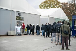 Am ehemaligen Flughafen Tegel stehen Geflüchtete Menschen vor einer Leichtbauhalle
