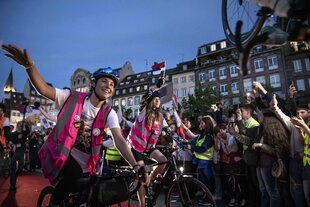 Junge Frauen auf Fahrrädern mit serbischen Fahnen, sie werden begrüßt von einer Mensge