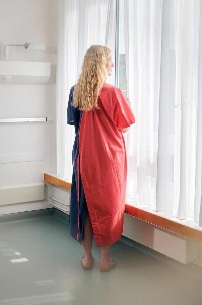 Eine Frau steht in einem blau-roten Flügelhelm an einem FEnster
