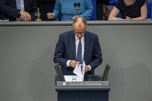 Friedrich Merz steh am Rednerpult im deutschen Bundestag und blättert in seinen Unterlagen