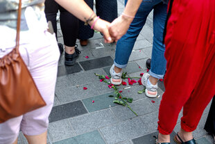Frauen halten sich an den Händen, Füße stehen auf am Boden liegende Rosen