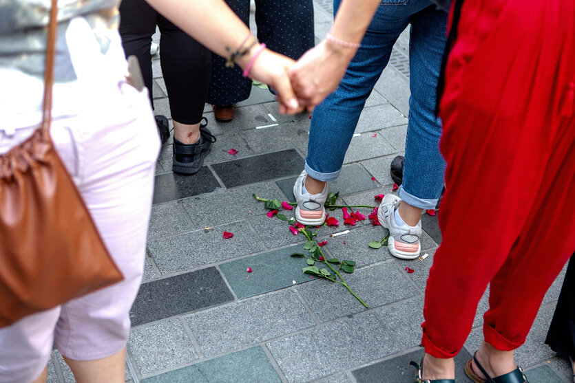 Frauen halten sich an den Händen, Füße stehen auf am Boden liegende Rosen